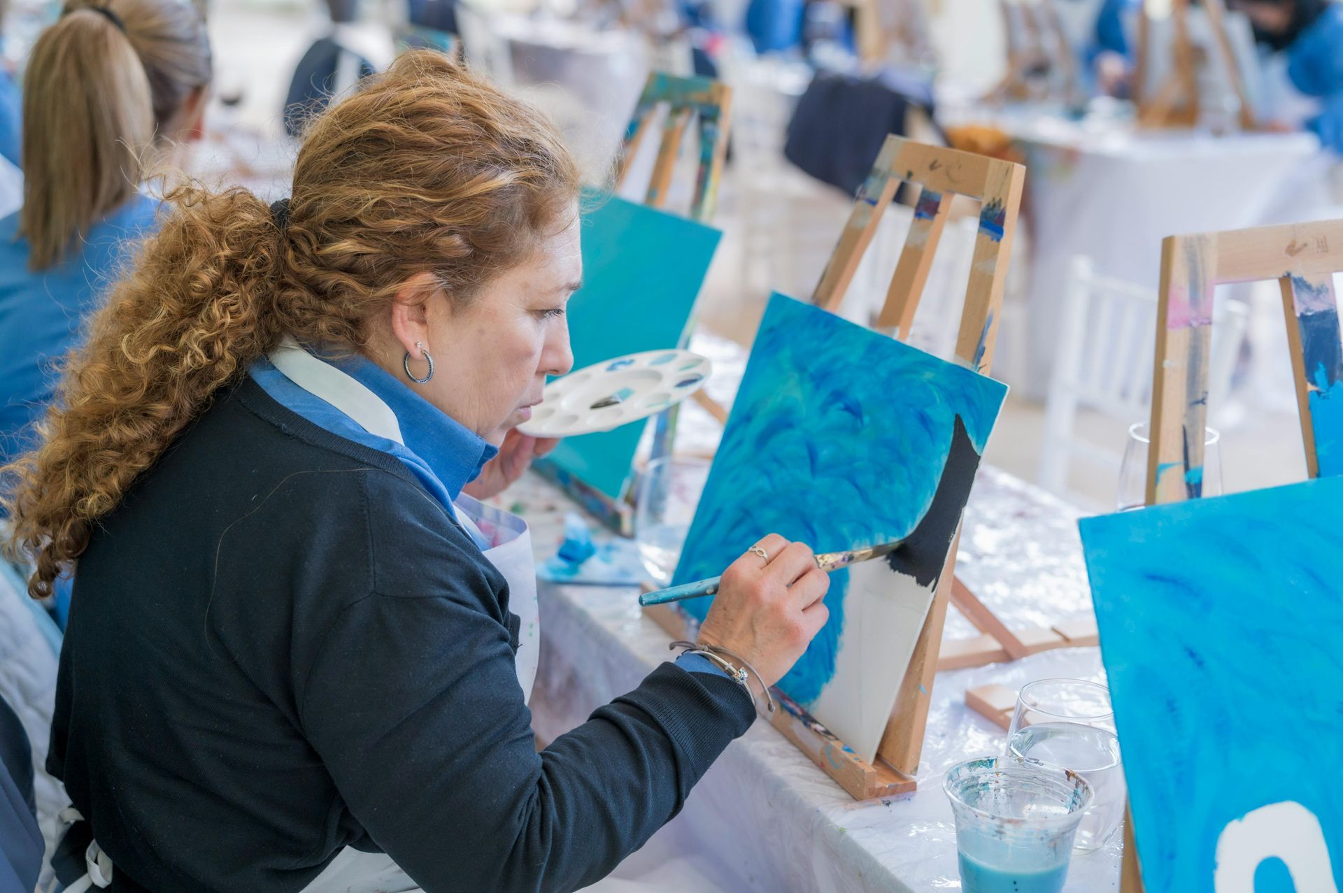 Person painting a bright blue canvas on an easel in an art studio