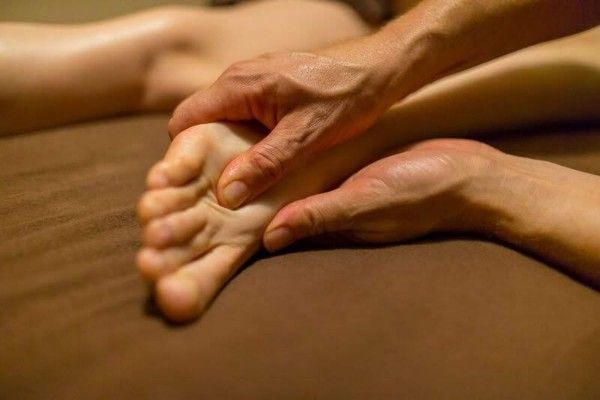 Hands massaging a person's foot on a brown bedspread