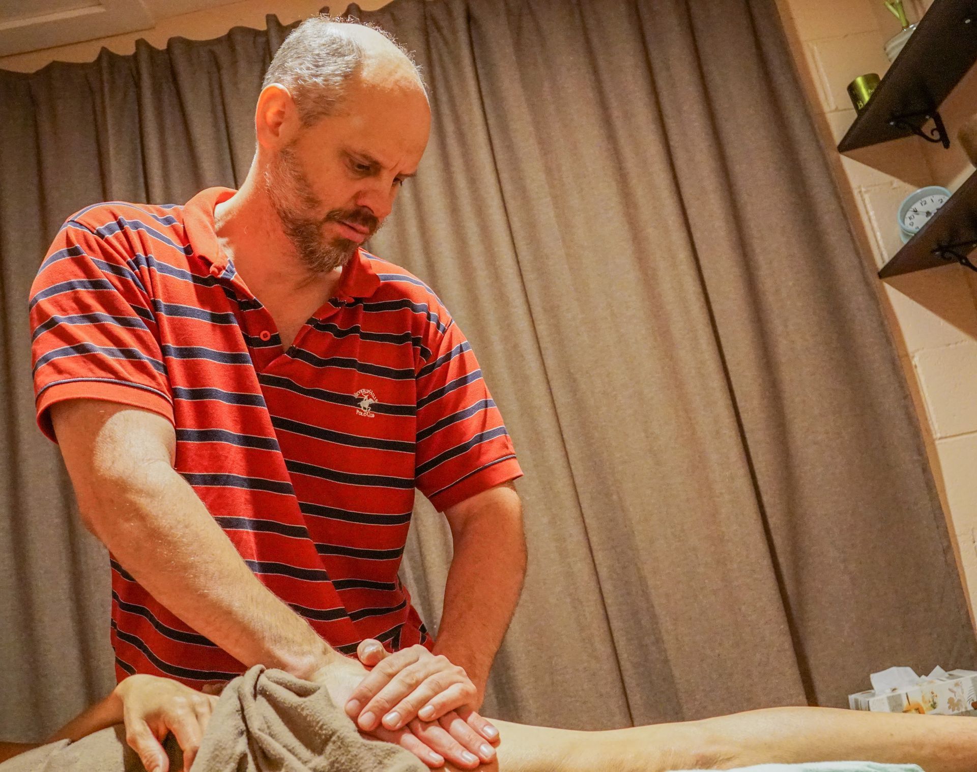 Massage therapist in a red striped shirt working on a client in a treatment room