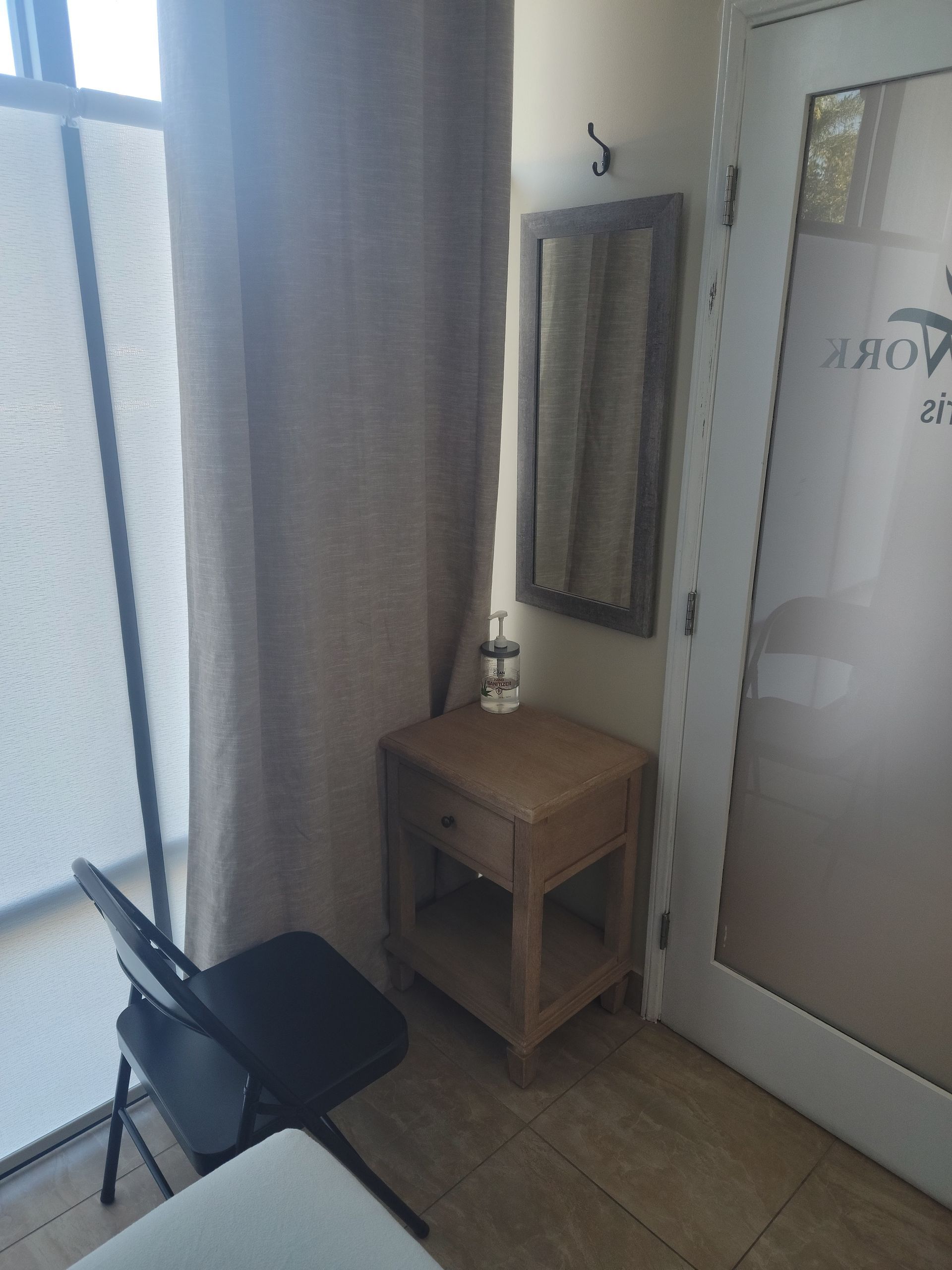 Small corner by a window with a black folding chair, wooden side table, mirror, and frosted glass door