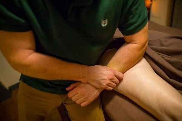 Person in green shirt massaging another person’s bent leg indoors