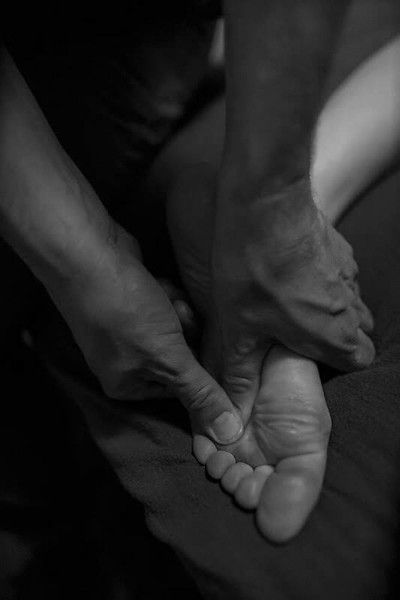 Hands massaging the sole of a foot on a dark background