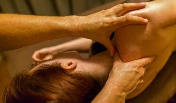 Hands and feet of two people in a close-up massage scene on a bed.