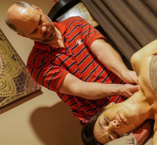 Two people in a room, one massaging the other's neck and shoulder while they lie on a couch.