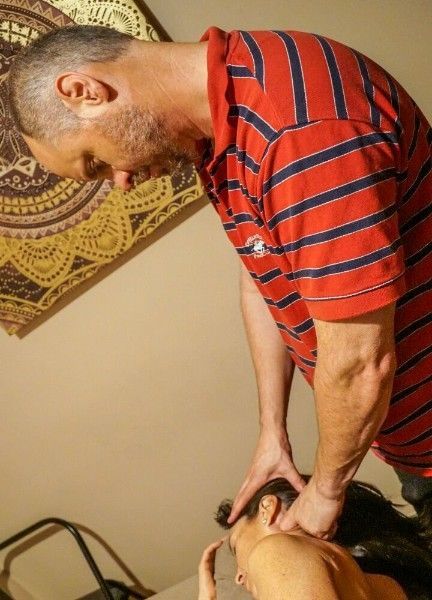Man in a red striped shirt leaning over and working on another person's head in a room