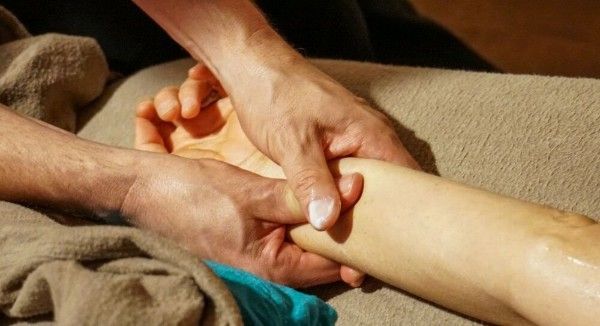 Hands massaging a person's lower leg on a beige couch
