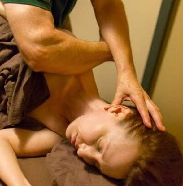 Person receiving a neck massage while lying on a brown cushion, eyes closed.