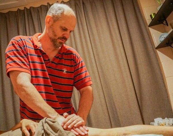 Man in a red striped shirt giving a massage on a table in a curtained room