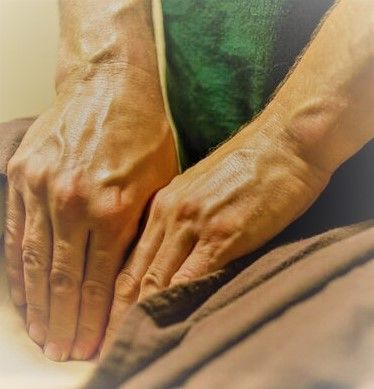 Hands pressing into a person’s back during a massage, with a green shirt in view