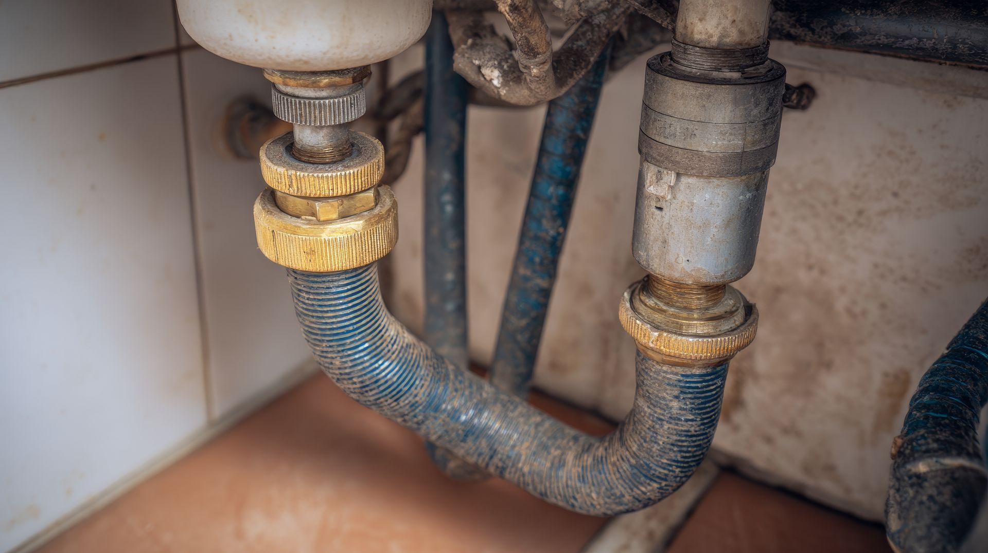 Flexible water supply hoses under a sink with corrosion and traces of leakage around the fittings 