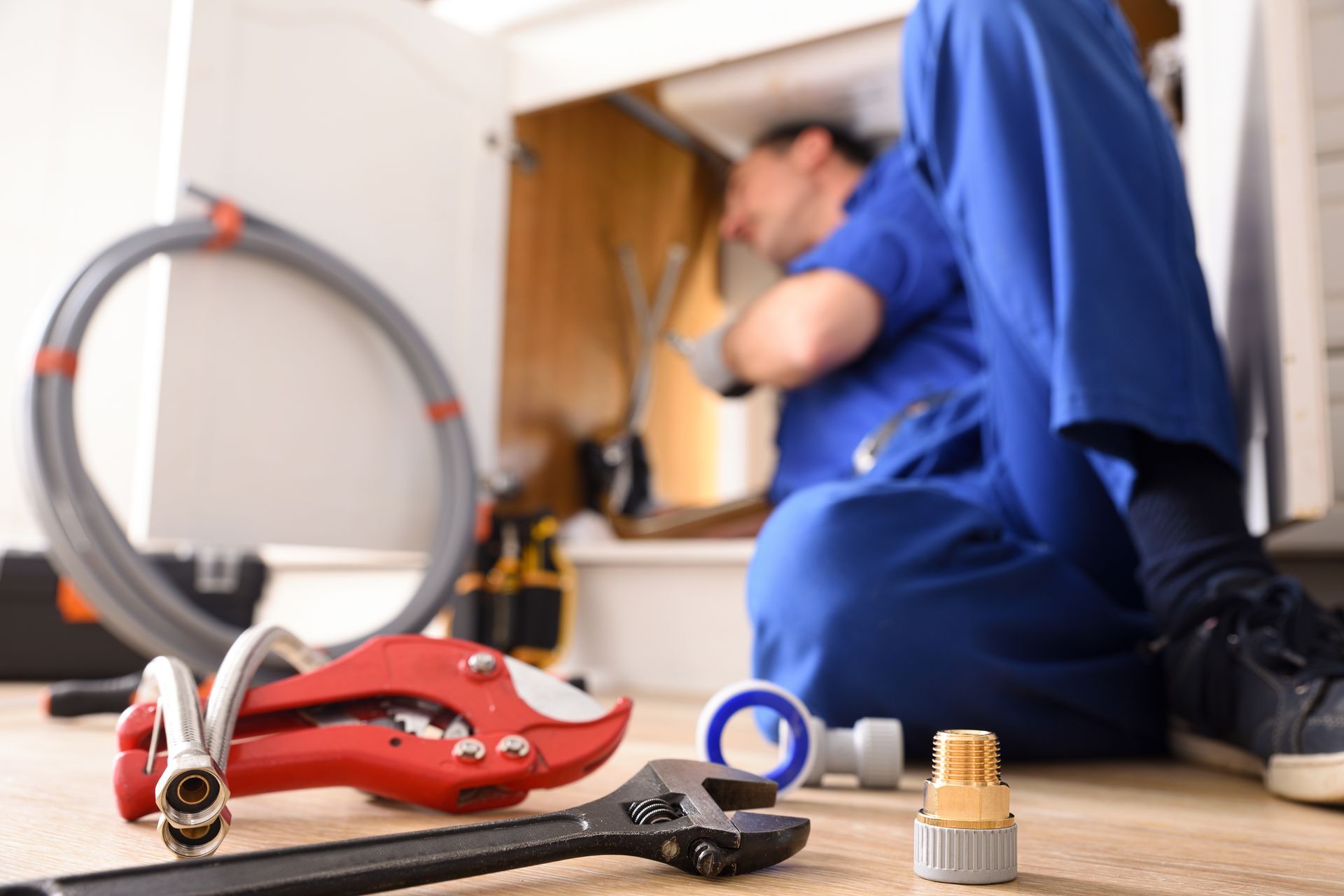 A plumber in a blue uniform working under a sink with tools nearby.