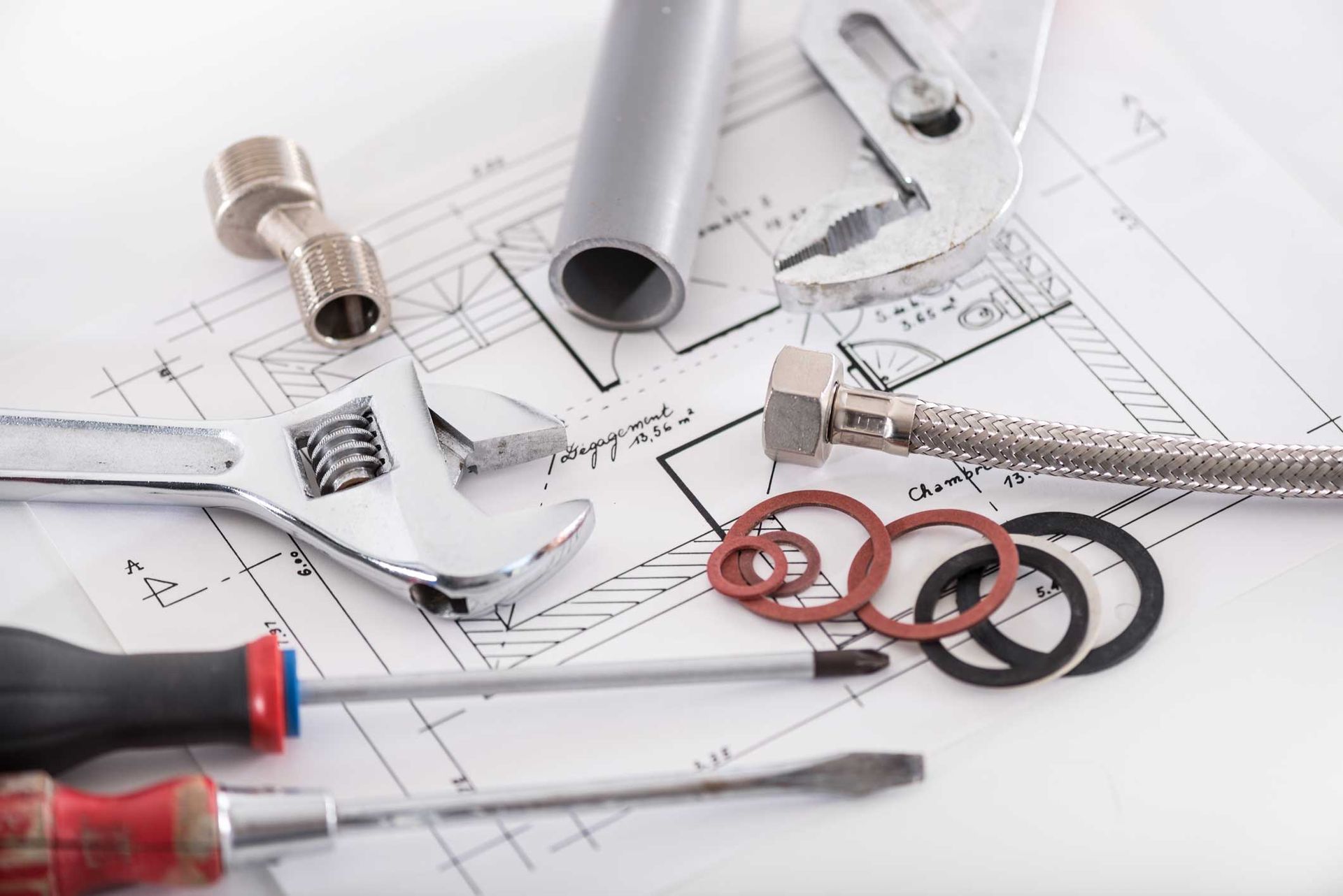 Plumbing tools and fittings on blueprints, including a wrench, pipes, and screwdrivers