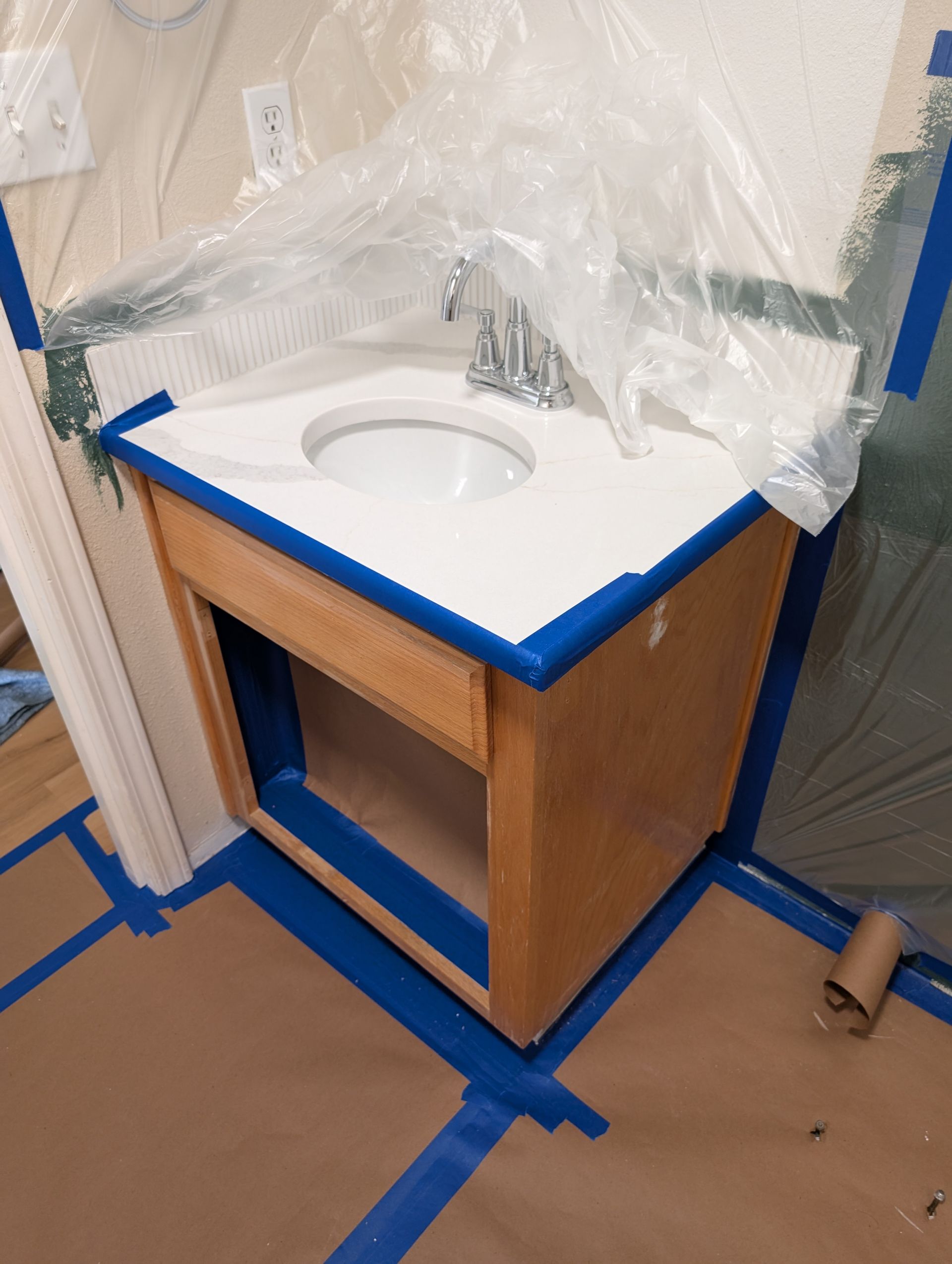 Bathroom vanity sink under construction, wrapped in plastic with blue painter’s tape around the cabinet.