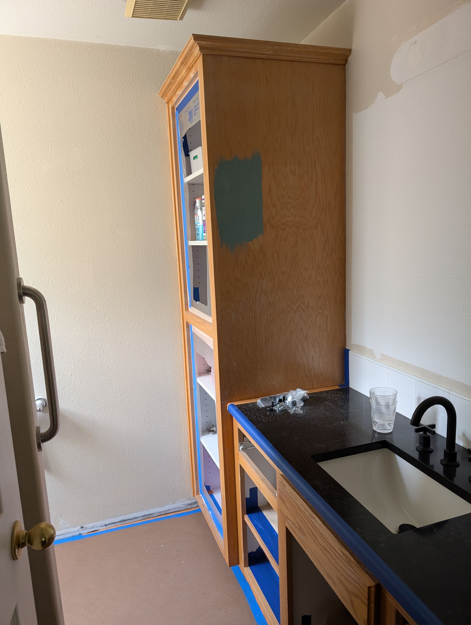 Small bathroom with wooden cabinet, black countertop sink, and partially painted walls undergoing renovation