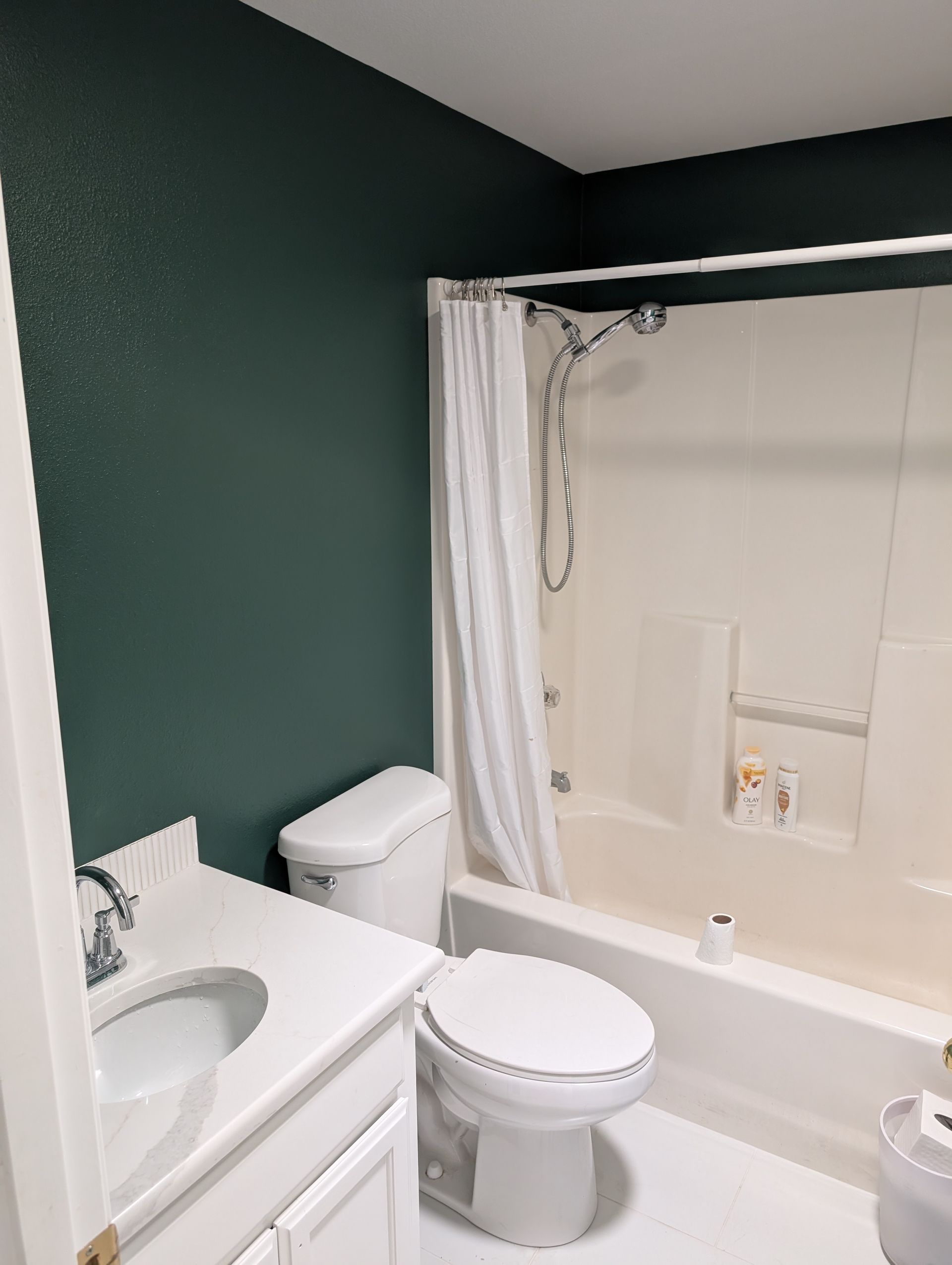 Small bathroom with a bathtub shower, toilet, sink, and dark green walls
