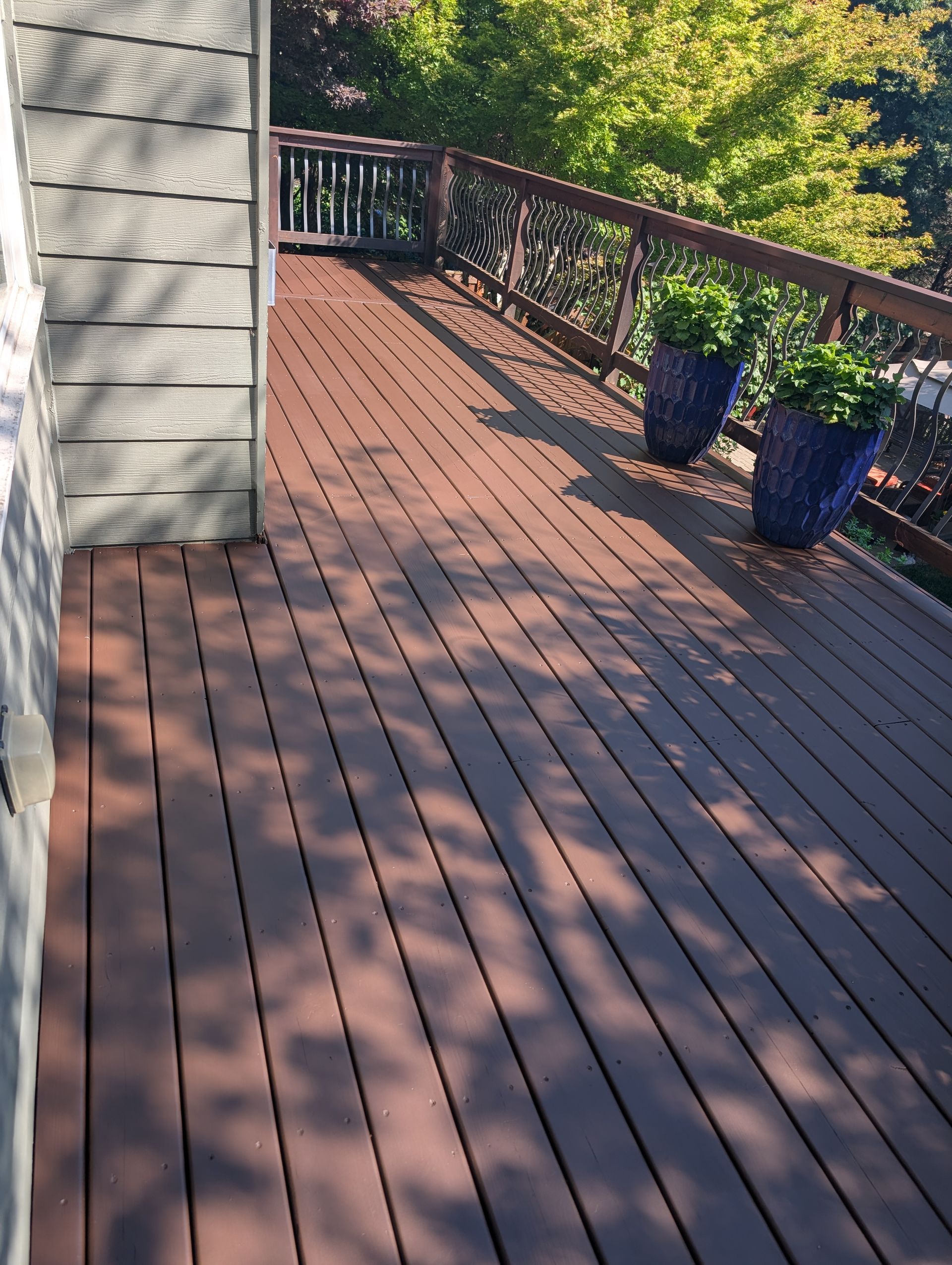 Wooden deck with potted plants beside a stone wall, lit by warm sunlight.
