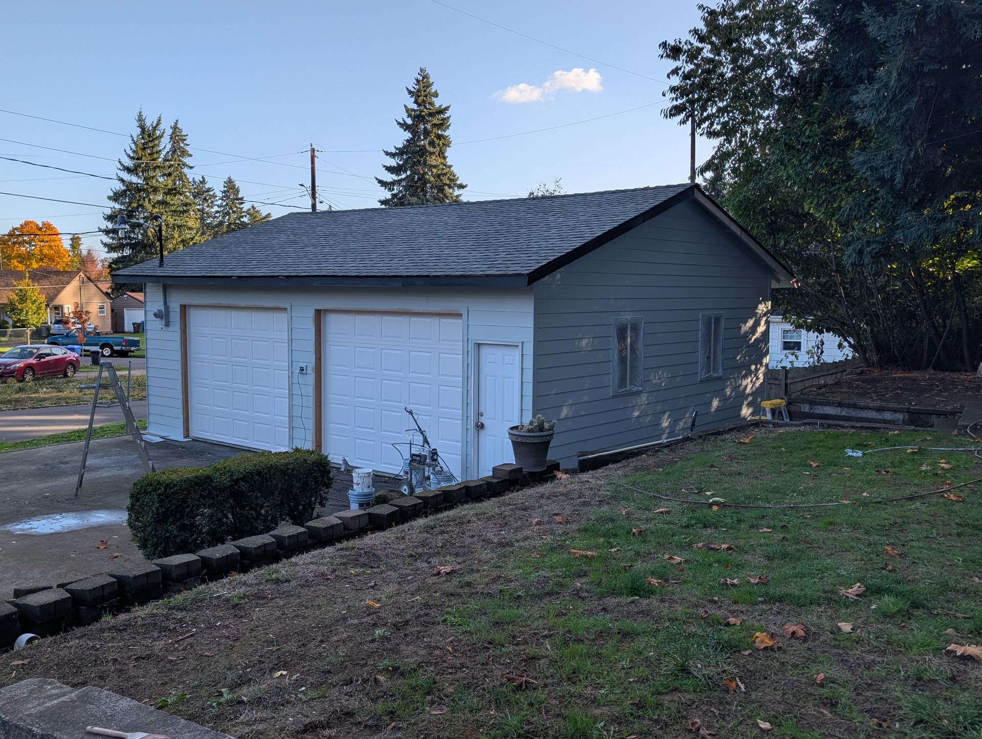 Small gray garage with white doors beside a grassy yard at dusk