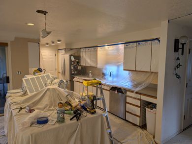 Cluttered kitchen with cabinets, countertops, appliances, and a partially covered table in the foreground.