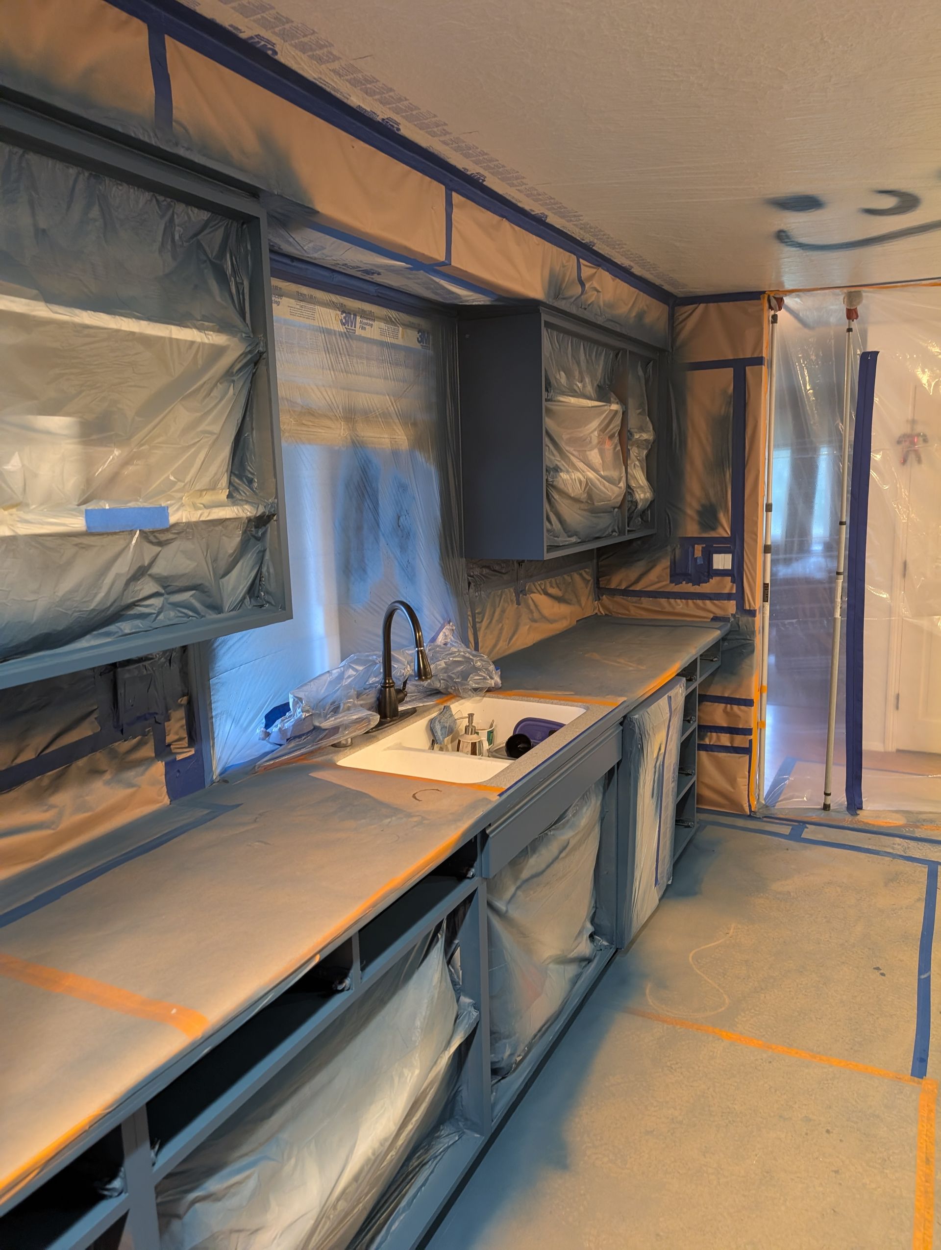 Blue kitchen with countertops, sink, cabinets, and a refrigerator, viewed from one end toward a doorway.