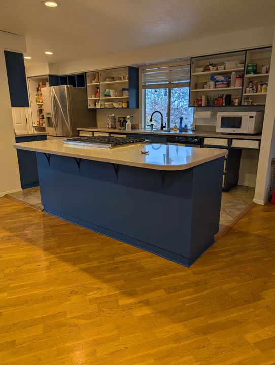 Modern kitchen with a large blue island, white countertop, and open shelving by a window