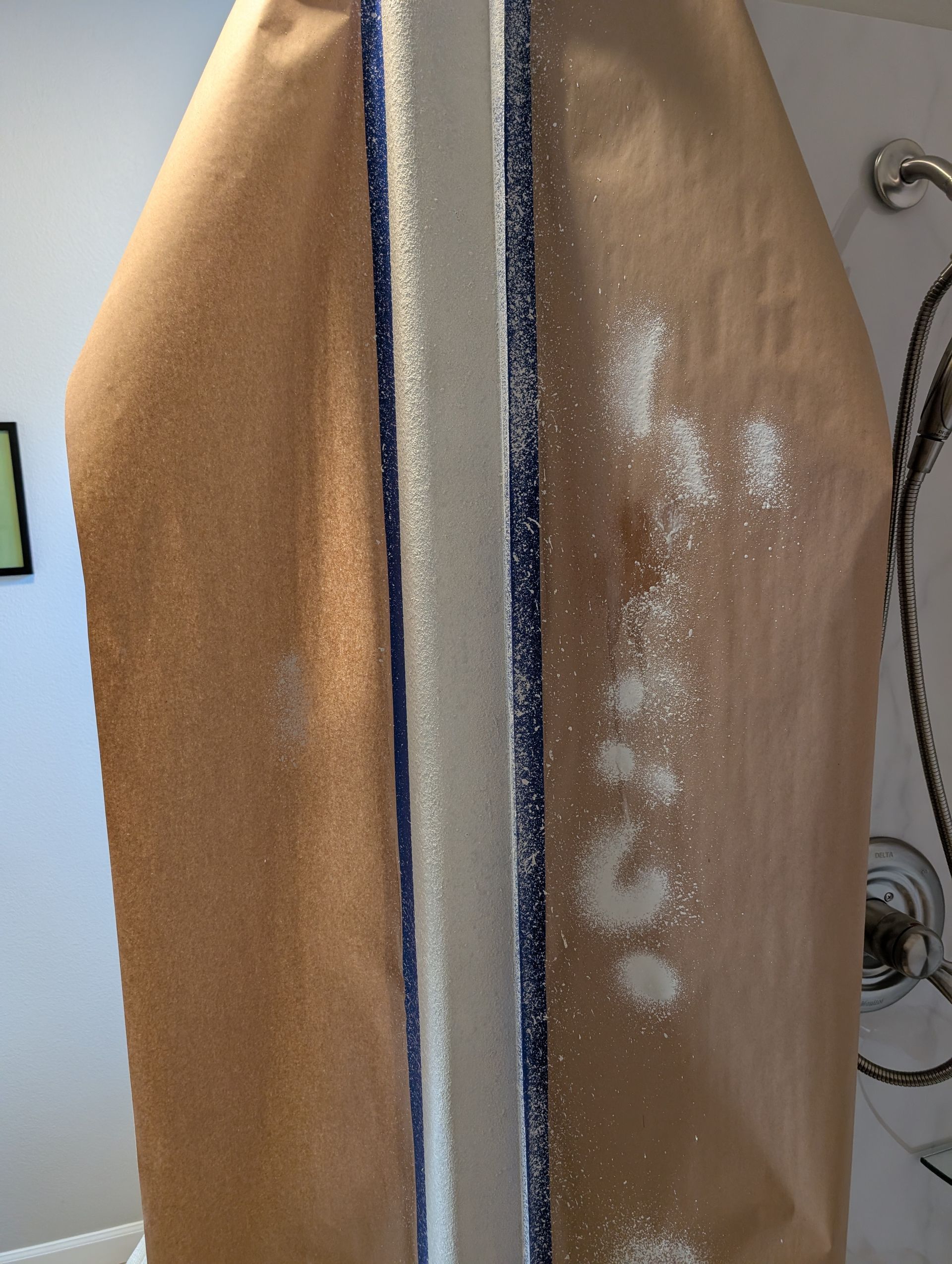 Two surfboards leaning upright, one tan and one brown with white patches, in a shower area