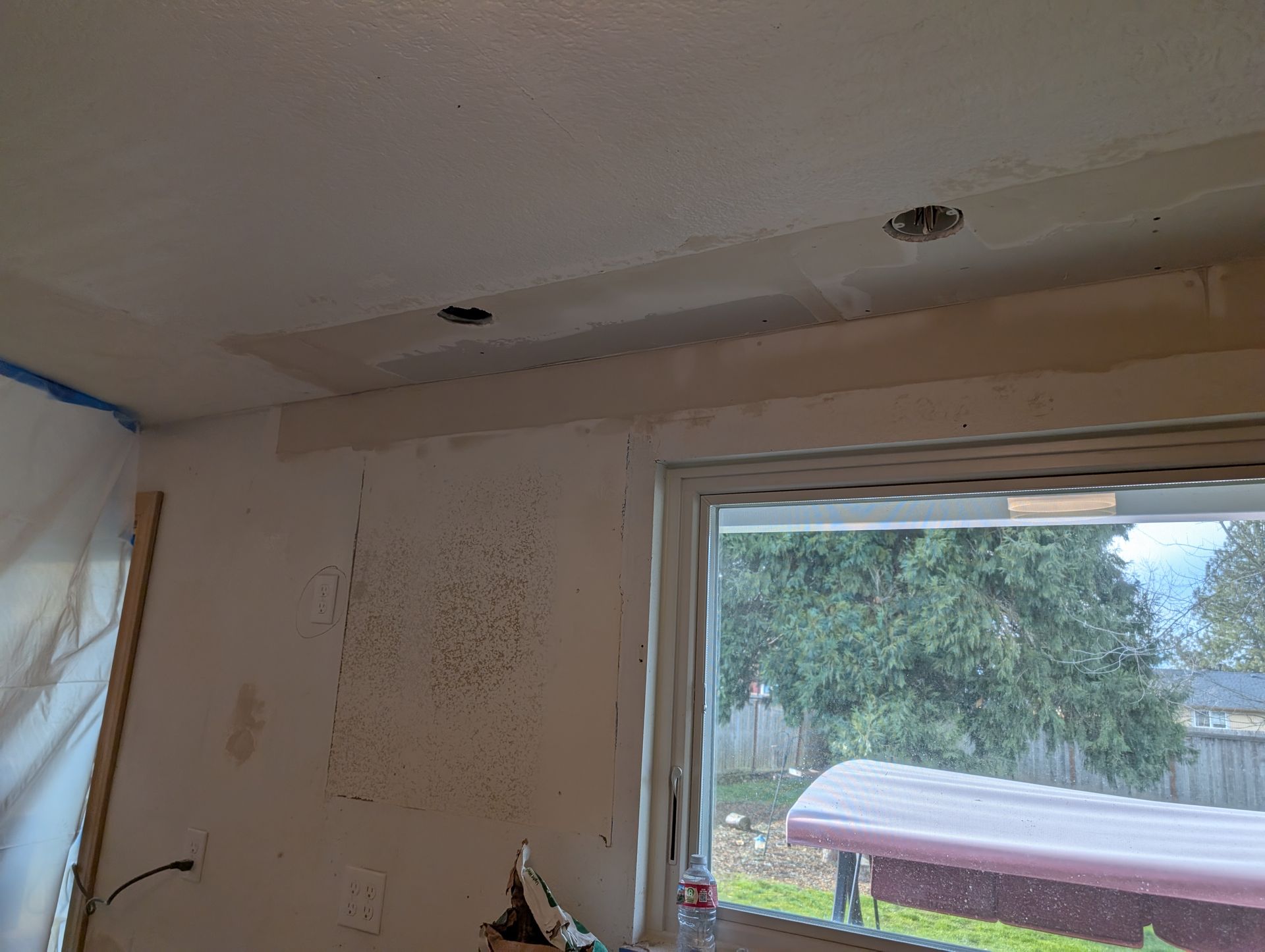 Partially finished room with white walls, ceiling cutouts, and a large window overlooking a yard