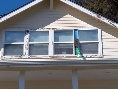 Windows on a beige house gable, with a blue vertical sign between the right windows.