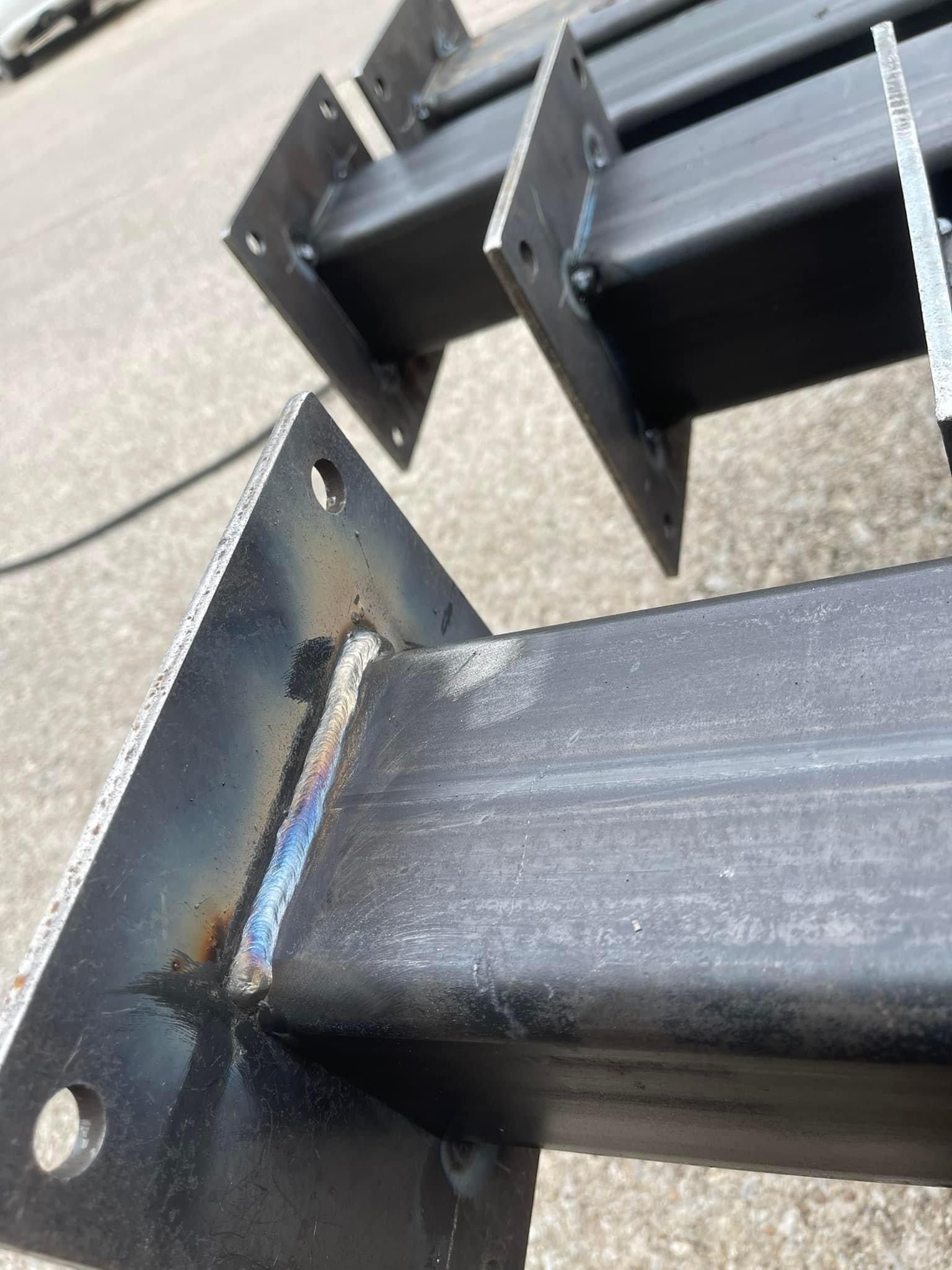 Black metal beams with welded triangular brackets on a concrete surface.
