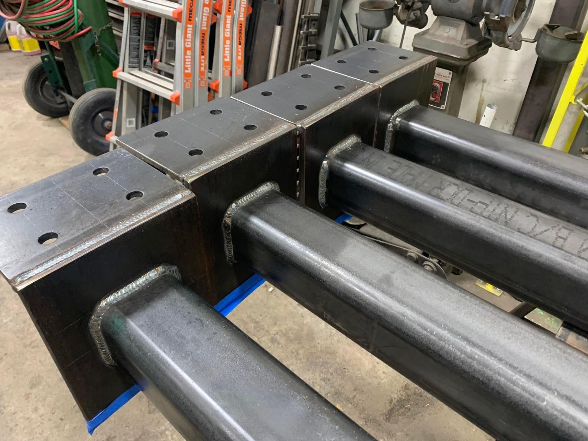 Black steel beams fitted into a large industrial machine frame with bolts and blue spacers