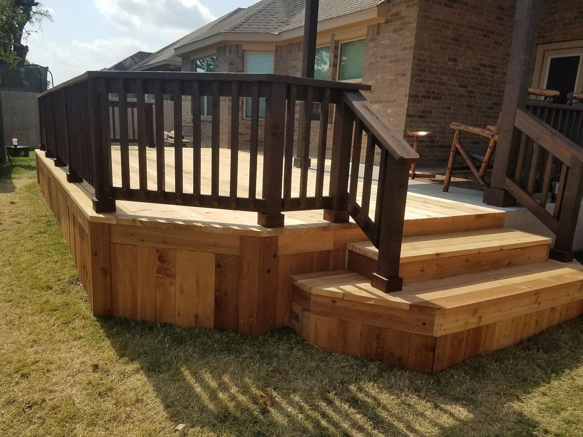 Wooden backyard deck with steps, black railings, and a small ramp beside a brick house.