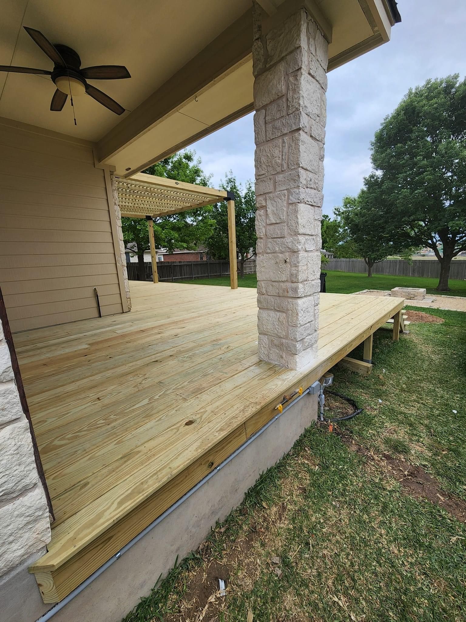 Covered porch with white brick columns, wooden floor, ceiling fan, and grassy yard beyond.