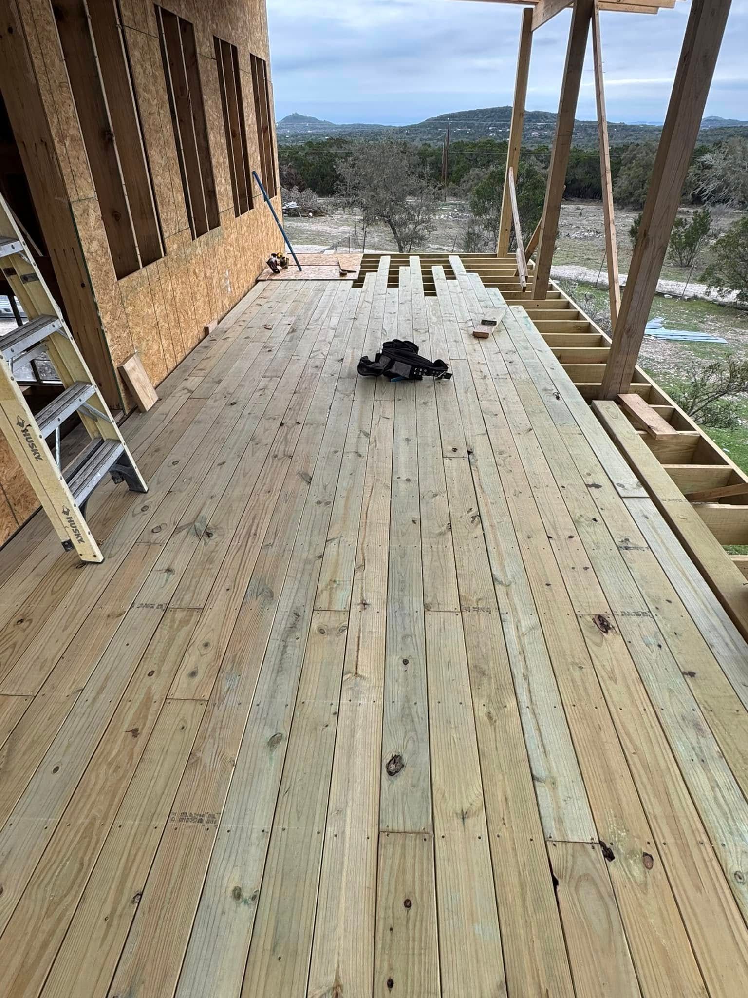 Wooden porch under construction with tools on the floor and a hillside view beyond the railing