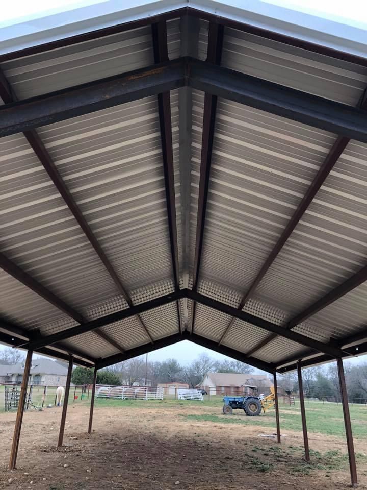Open-sided metal carport with a peaked roof over a dirt lot outdoors