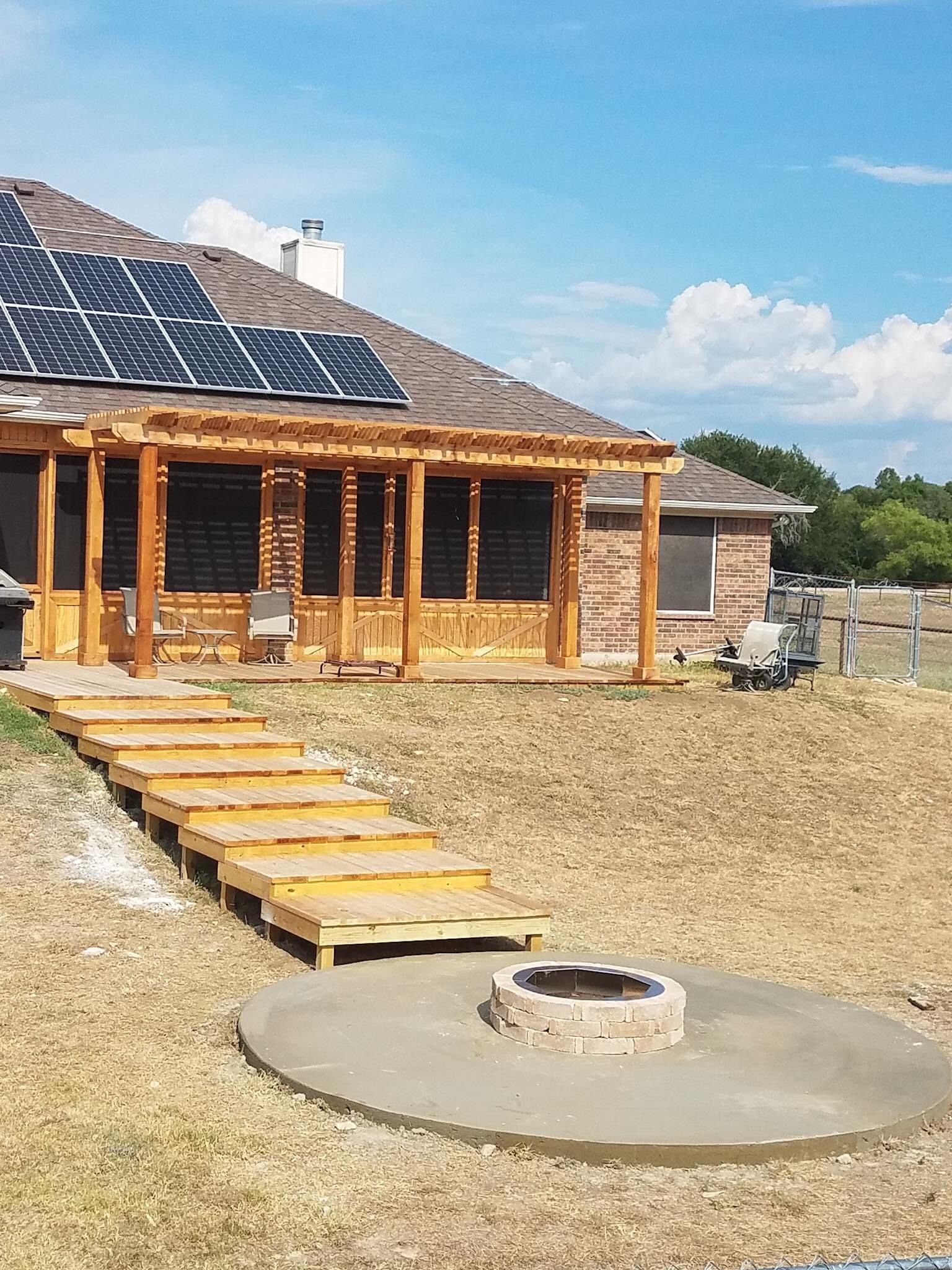 Wooden cabin with solar panels, a gravel yard, and a fire pit under a clear sky.