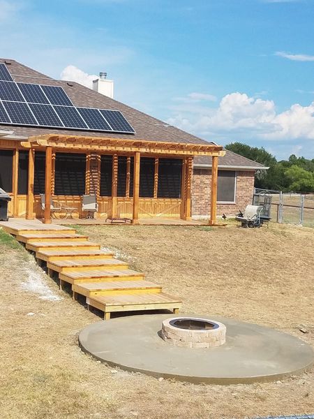 Wooden cabin with solar panels, gravel yard, and a circular fire pit in the foreground.