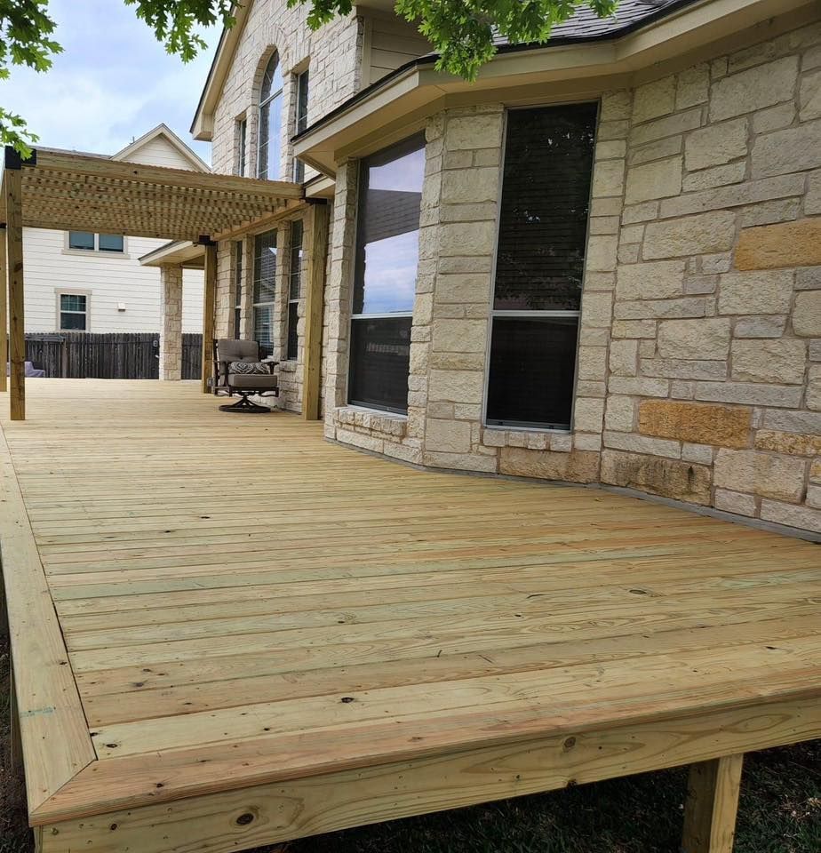 Wooden deck beside a stone house with covered pergola and large windows