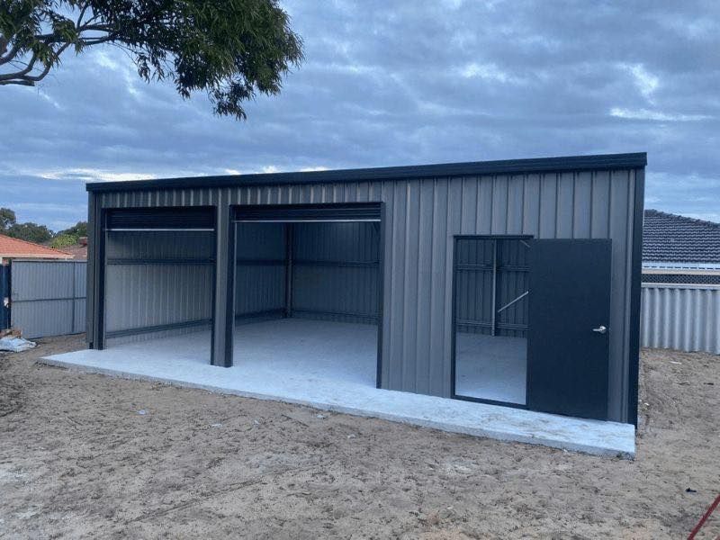 New steel shed with open bays and a dark door, set on a gravel lot under cloudy sky