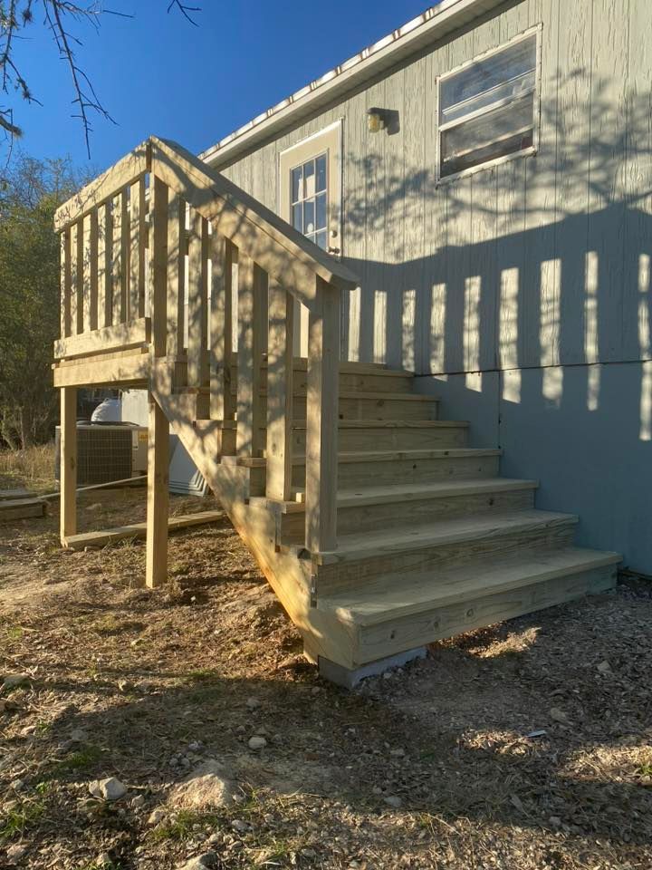 Wooden exterior stairs with railing leading to a beige house in a wooded yard