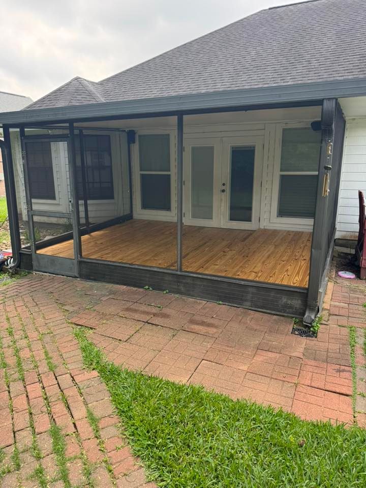 Covered front porch with black railings, wood floor, and white double doors on a brick patio.