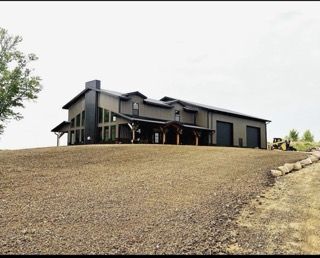 Dark modern house on a gravel hill under a cloudy sky, with a porch and garage on the right.