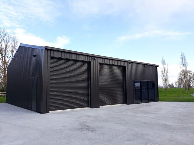 Black industrial warehouse with large roll-up doors on a concrete lot under a blue sky