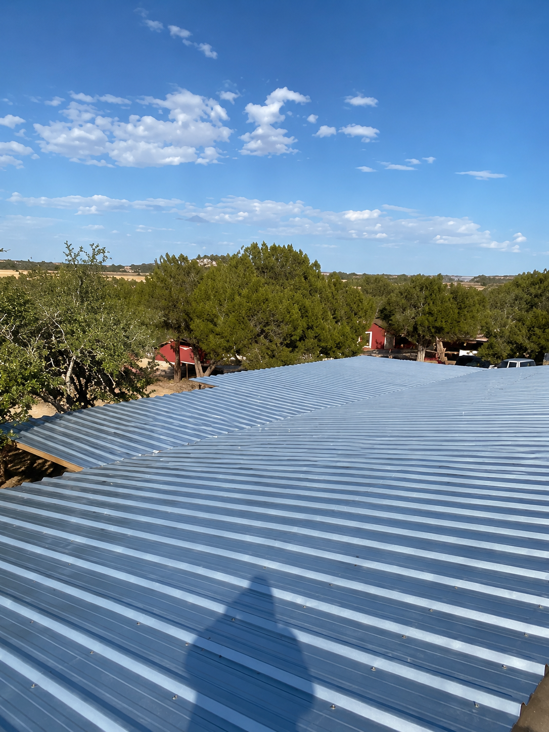 Corrugated metal rooftop with tree shadows under a blue sky with scattered clouds