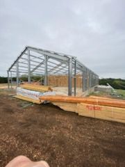 Partially built steel-frame barn on a muddy lot under cloudy skies