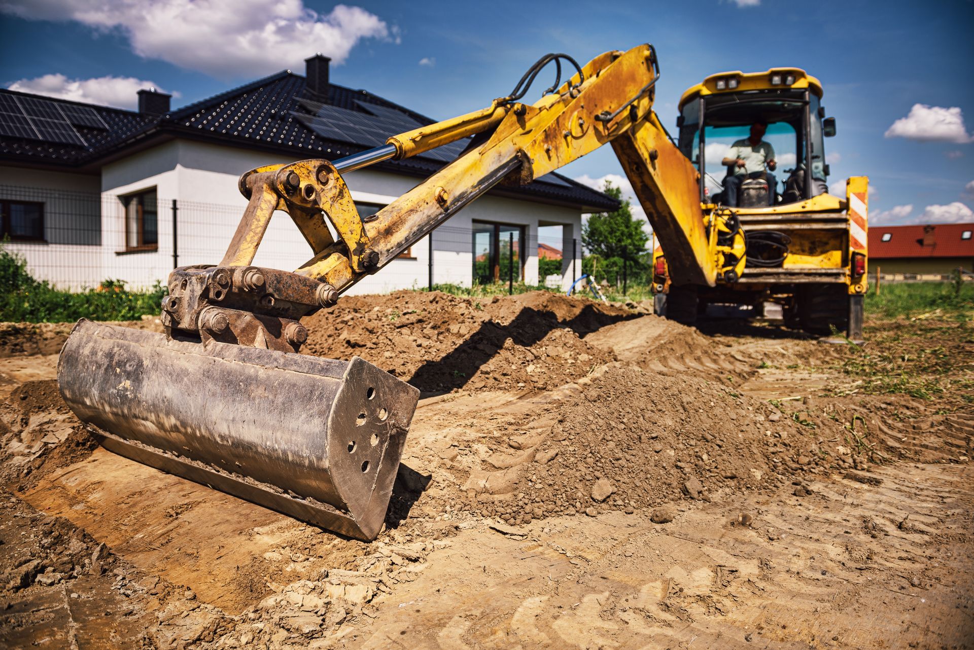 Yellow excavator leveling dirt in front of a house under construction