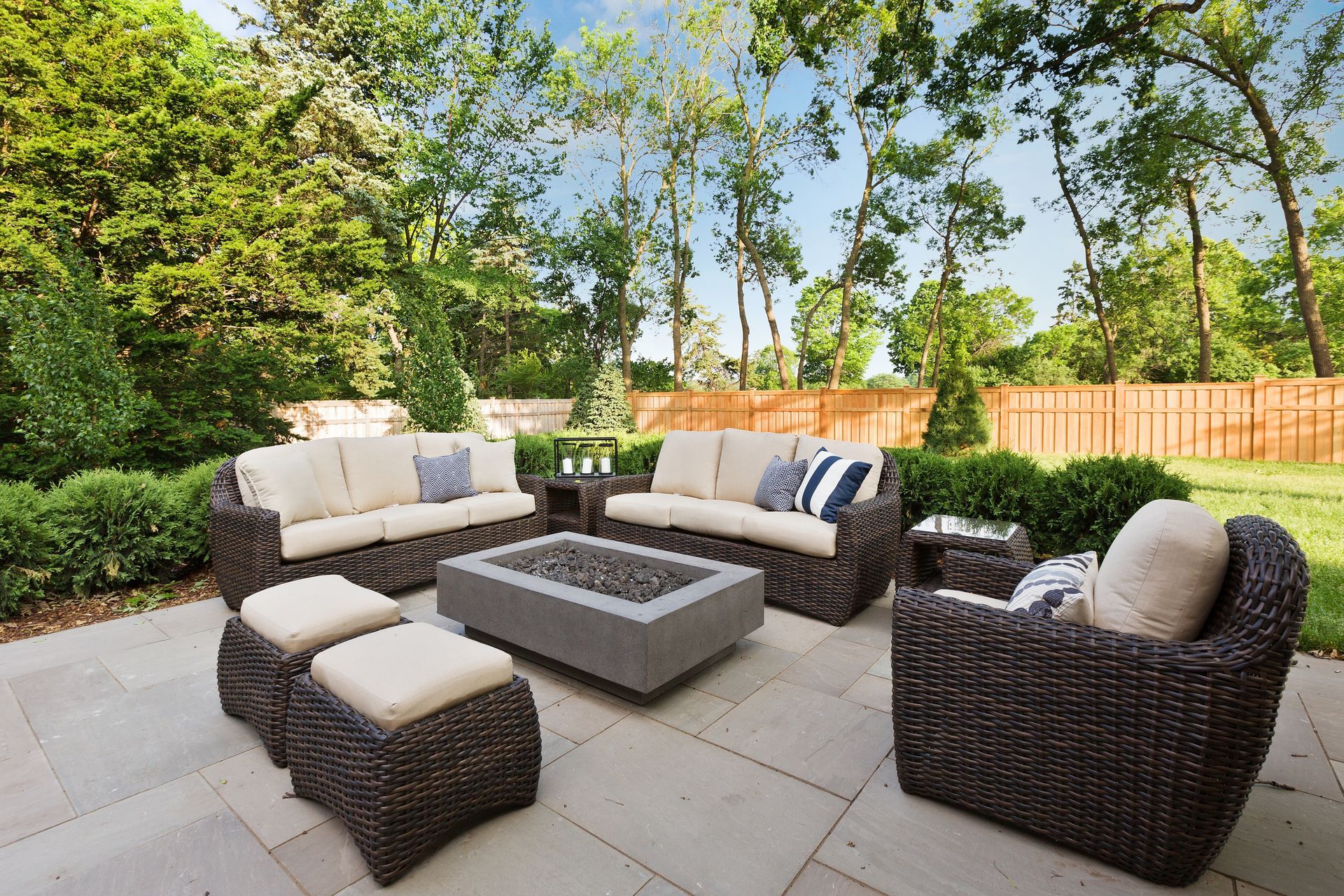 Patio seating area with dark wicker furniture, light cushions, and a square fire pit on stone pavers