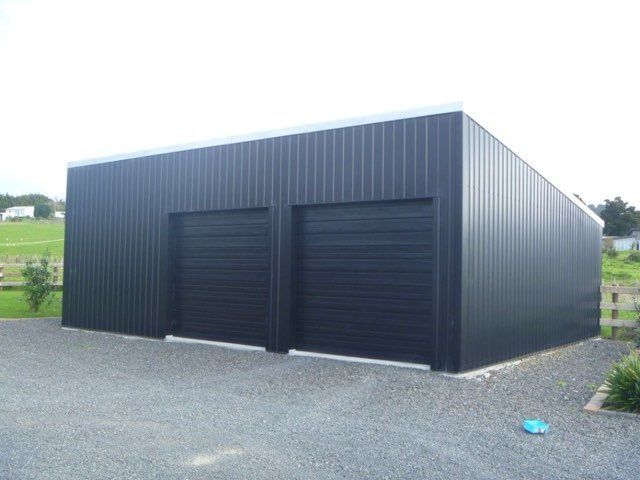 Dark gray metal garage with two roll-up doors on a gravel lot