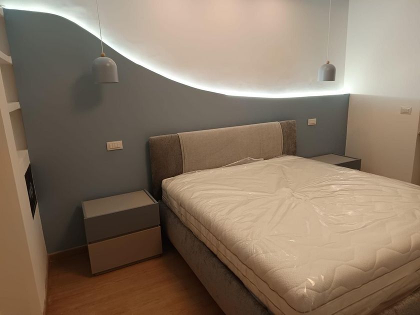 Cucina moderna con mobili in legno, ripiani bianchi e lampade a sospensione nere.