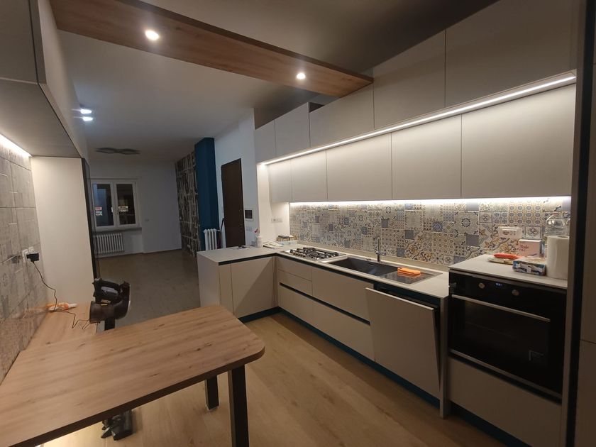 Cucina moderna con mobili in legno, ripiani bianchi e lampade a sospensione nere.