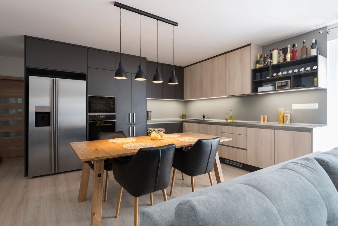 Cucina moderna con mobili in legno e neri, frigorifero in acciaio inox, tavolo da pranzo, lampade a sospensione.