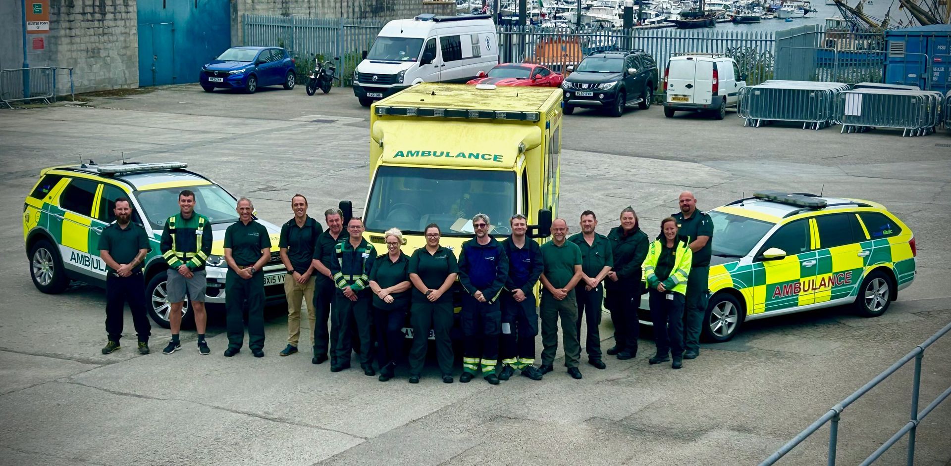 A group of emergency responders in uniform standing in front of an ambulance and two emergency response vehicles.